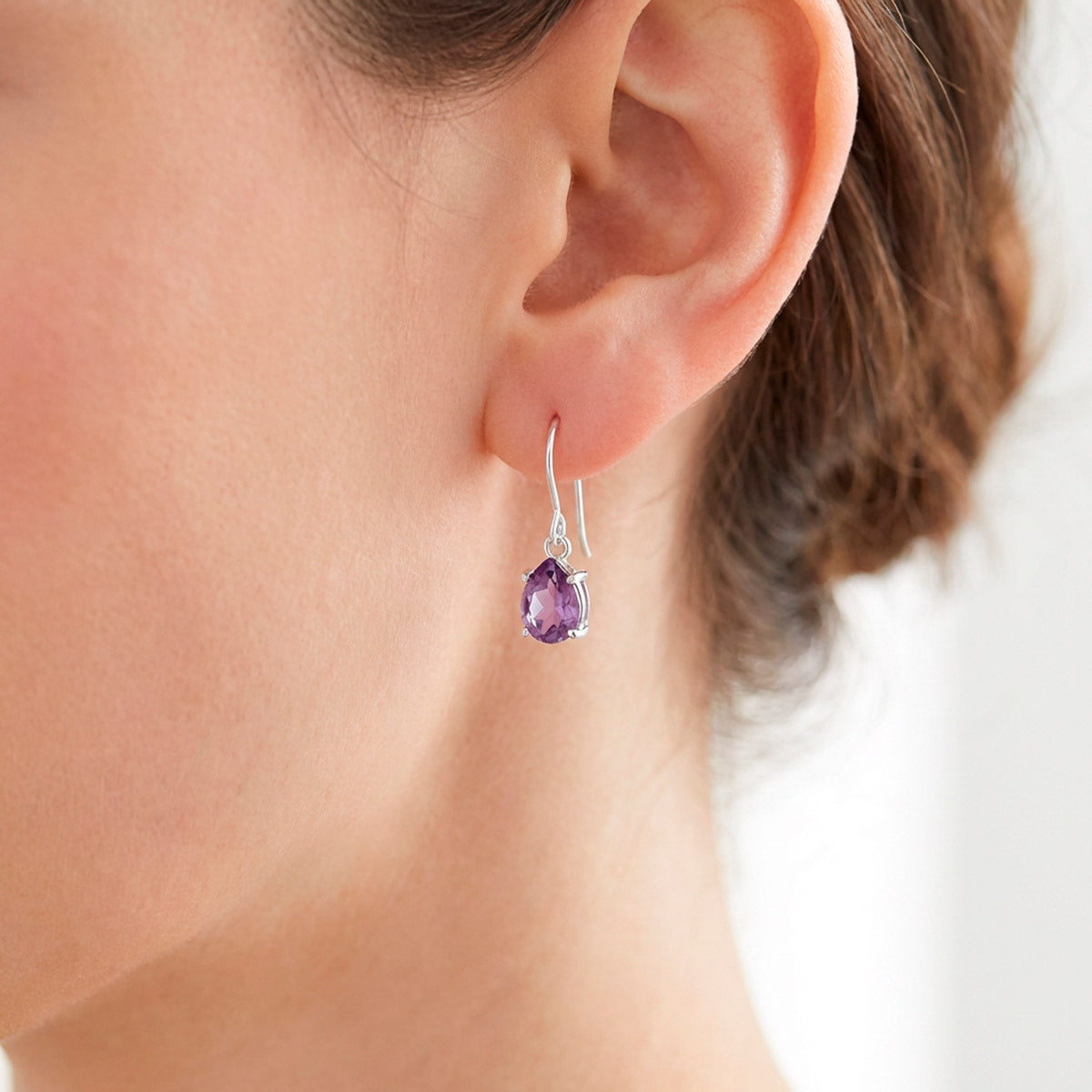 Hopeiset pisaranmalliset ametisti korvakorut naisen korvassa
